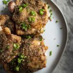 close up photo of crispy chicken thighs on a plate with diced chilies on top