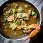 lousiana seafood gumbo with okra, seafood and sausage in roux in a bowl with crab claw