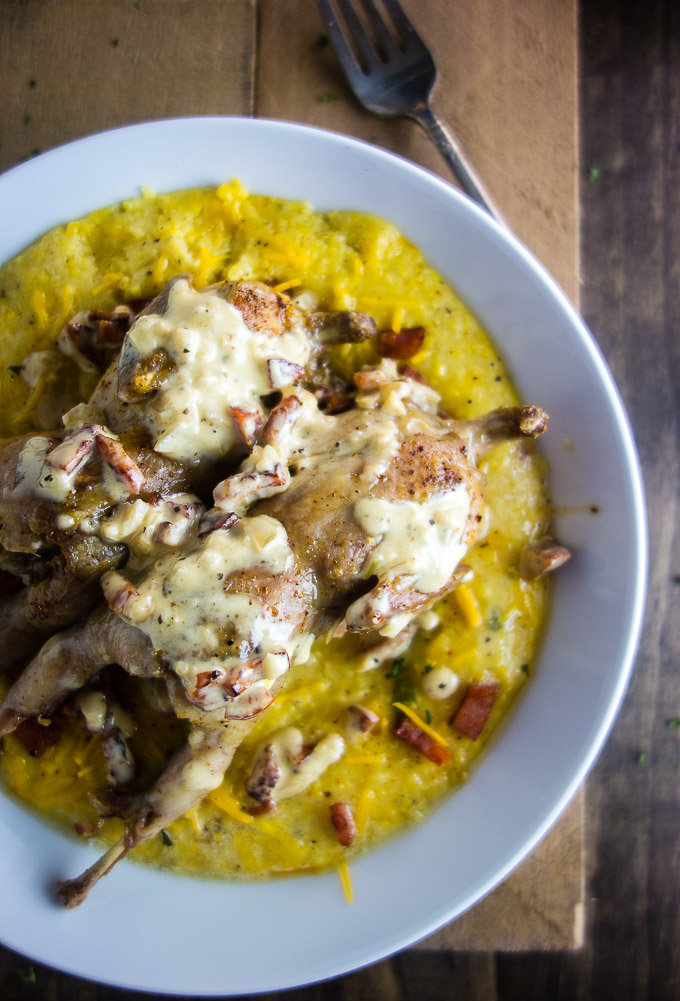 roast quail with andouille sausage cream sauce on top of grits in a bowl