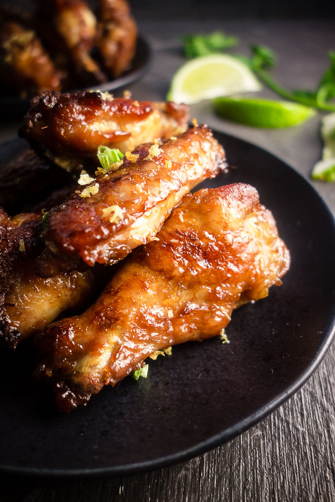 gooey chicken wings stacked on a plate with green onion