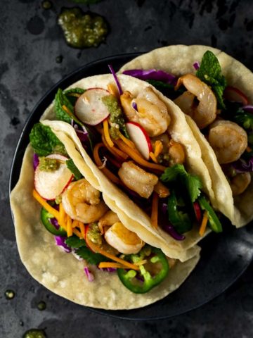 3 shrimp tacos on a plate with vegetables and salsa