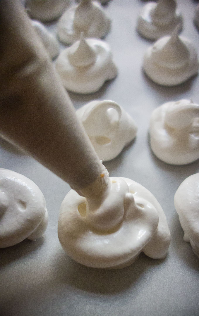 meringue being piped from a pastry bag onto a baking sheet