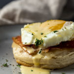 biscuit with bacon and egg on top drizzled in yellow sauce