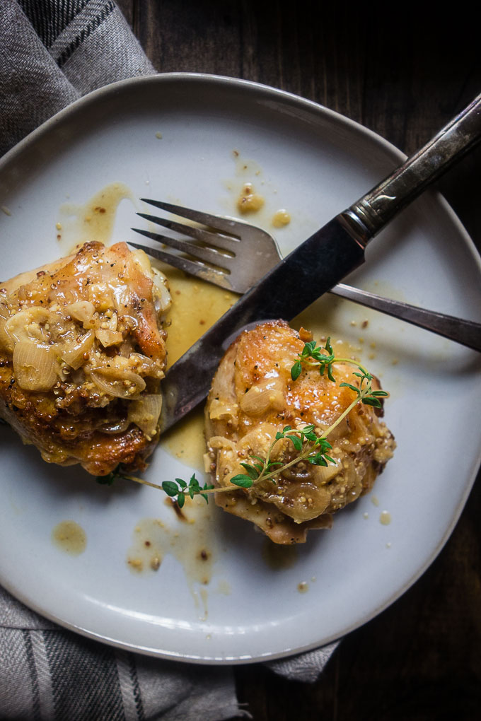 chicken thighs in white wine mustard sauce on a plate with fork and kmife