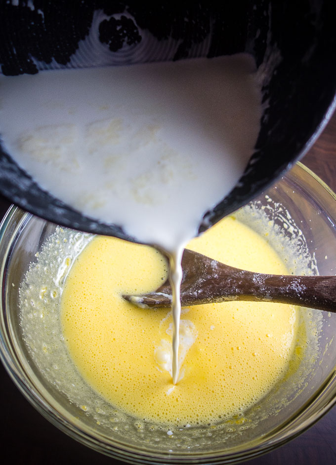 pouring cream from saucepan into bowl of custard