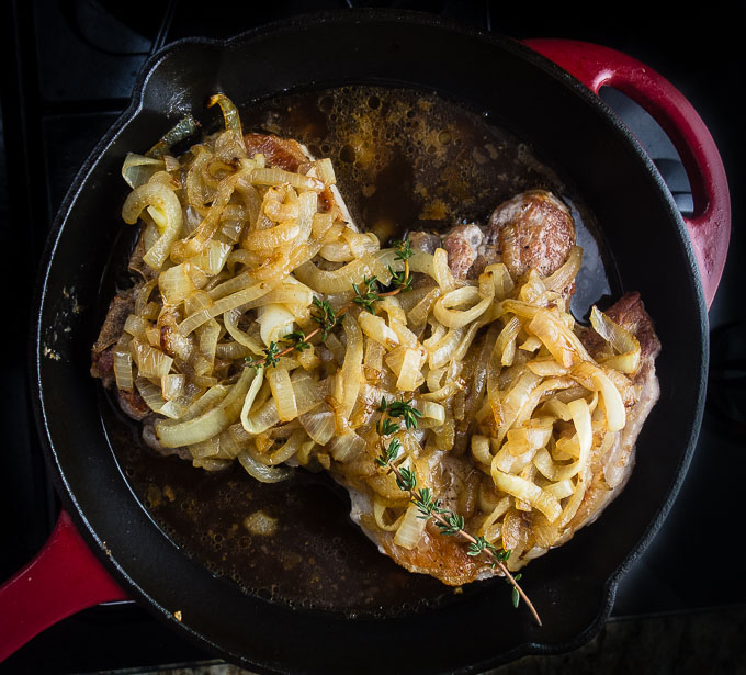 pork chops covered in onions and thyme in a skillet