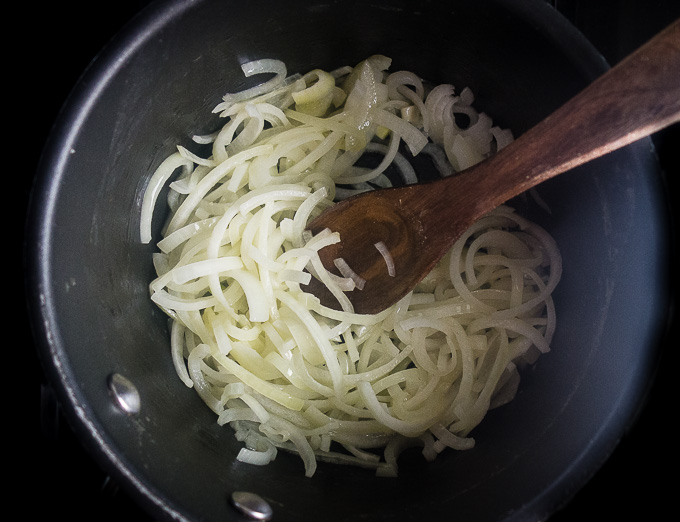 raw onions in a sauce pan with wooden spoon