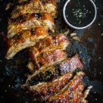 cut up ribs with side of sauce on baking sheet