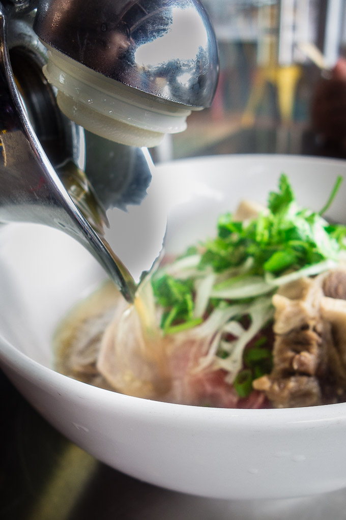 broth being poured into a bowl of meat and noodles