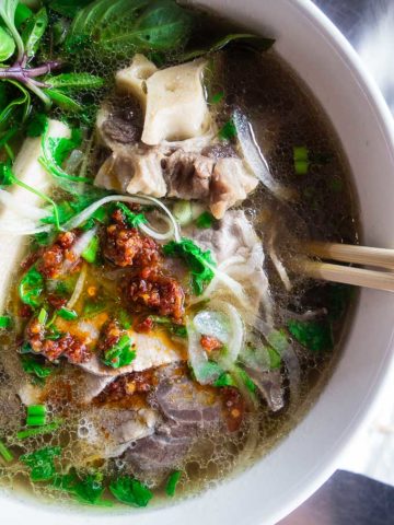 close up fo soup with meat and noodles and spicy chicli sauce