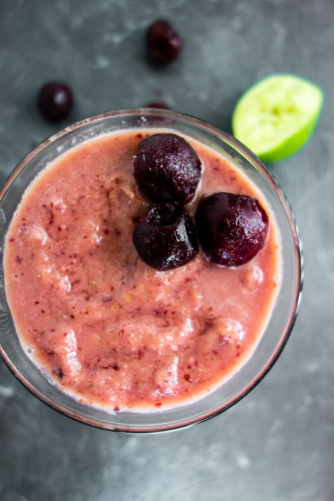 red smoothie with cherries on top and lime in background