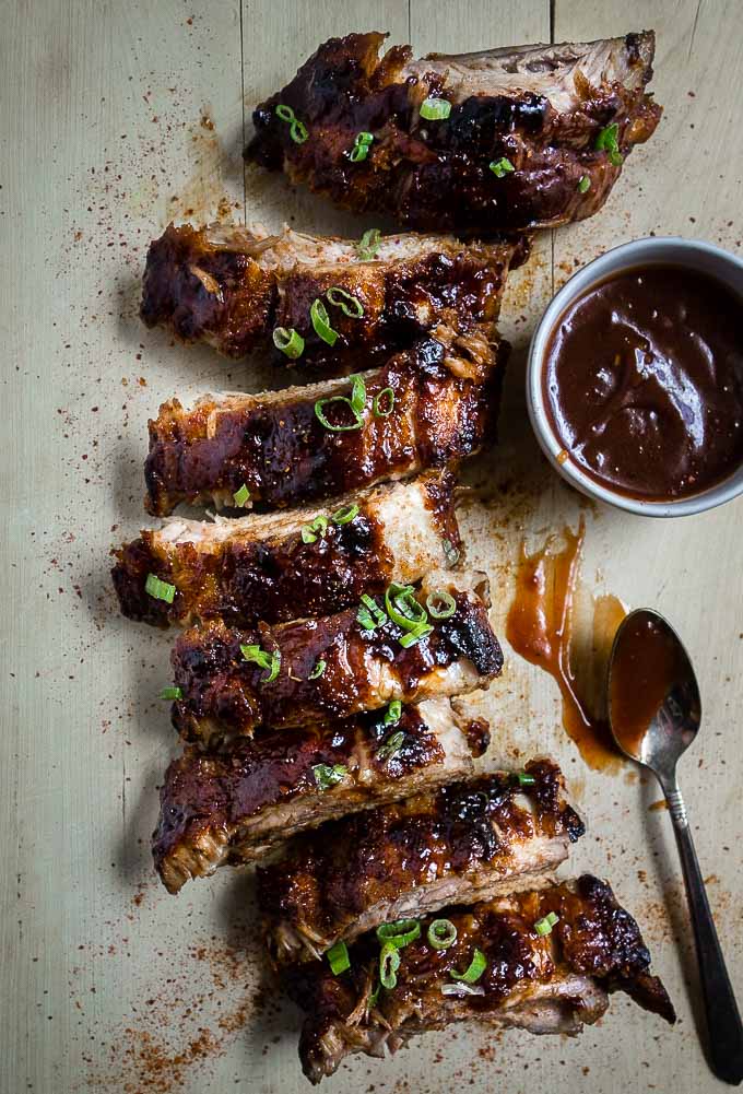 ribs on a cutting board with dish of sauce and spoon