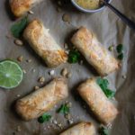 baked pad thai egg rolls on parchment paper garnished with peanuts and lime