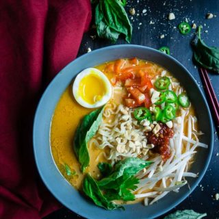 thai red curry ramen with fresh vegetables garnished with basil leaves and peanuts