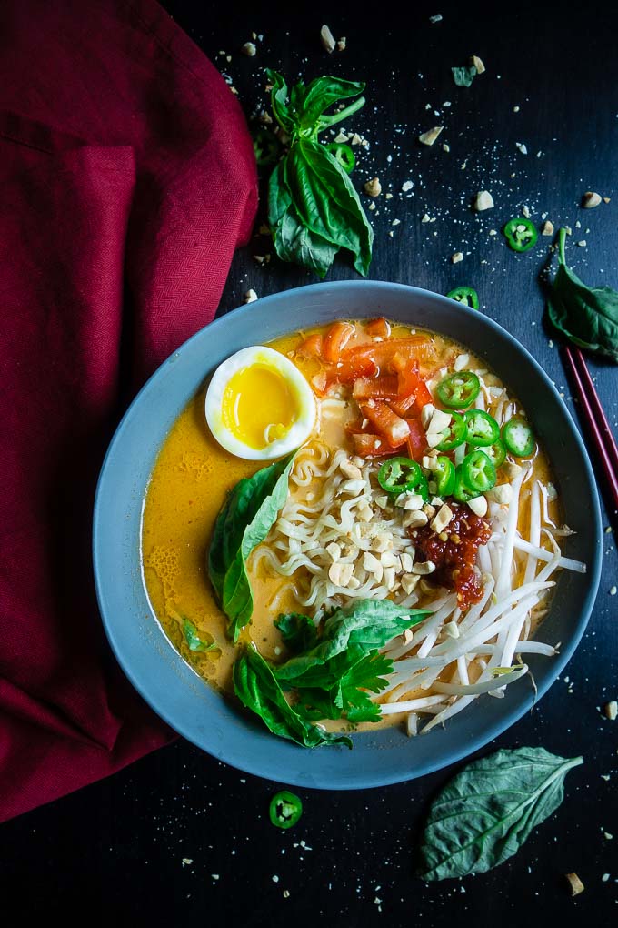 thai red curry ramen with fresh vegetables garnished with basil leaves and peanuts