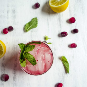 glass of sparkling cranberry lemonade garnished with mint, cranberries and lemon slices