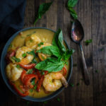 shrimp and vegetables with sauce in a bowl with a spoon and fresh herbs