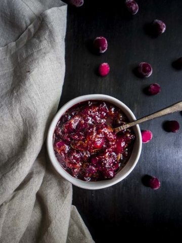 bowl of cranberry orange chutney with a spoon and fresh cranberries as garnish