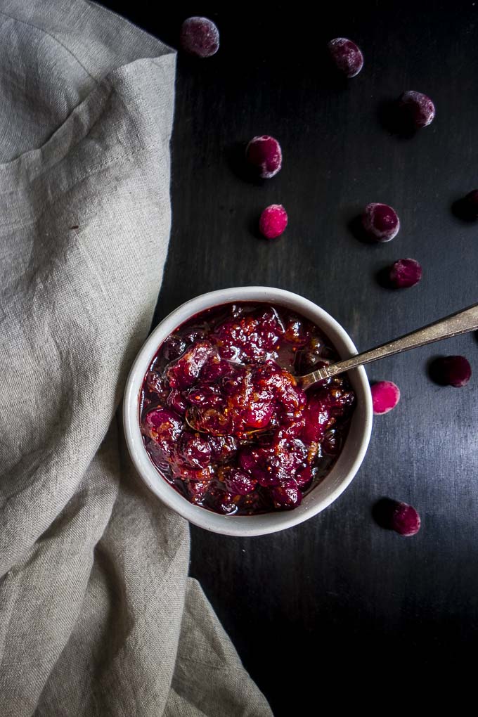 bowl of cranberry chutney with a spoon and fresh cranberries as garnish