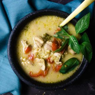 bowl of creamy soup with chicken, vegetables and garnished with basil and a gold spoon