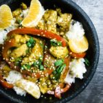 chicken pieces in sauce over rice with orange segments and sesame seeds