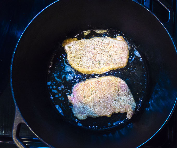 breaded pork cutlets being fried in a dutch oven