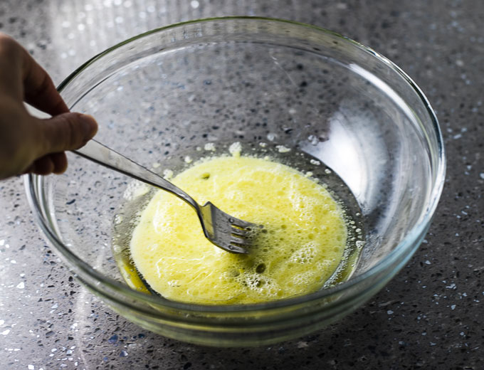 an egg being whisked with a fork in a bowl