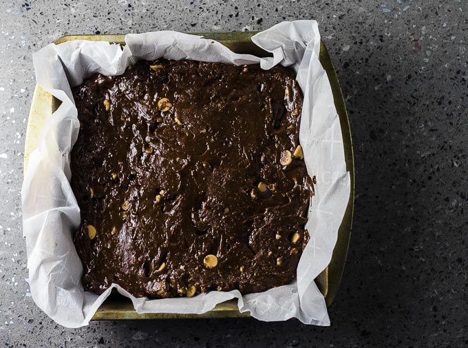 uncooked brownie batter in a square metal baking dish lined with parchment paper