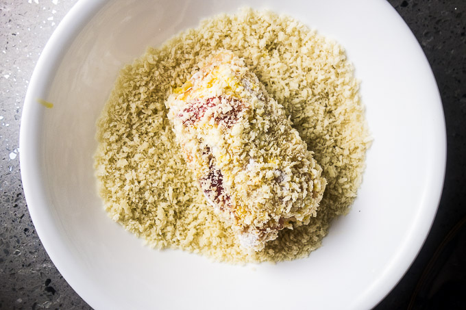 stuffed chicken roll being rolled in bread crumbs
