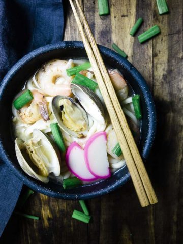bowl of udon noodle soup with clams, shrimp and green onions with chopsticks