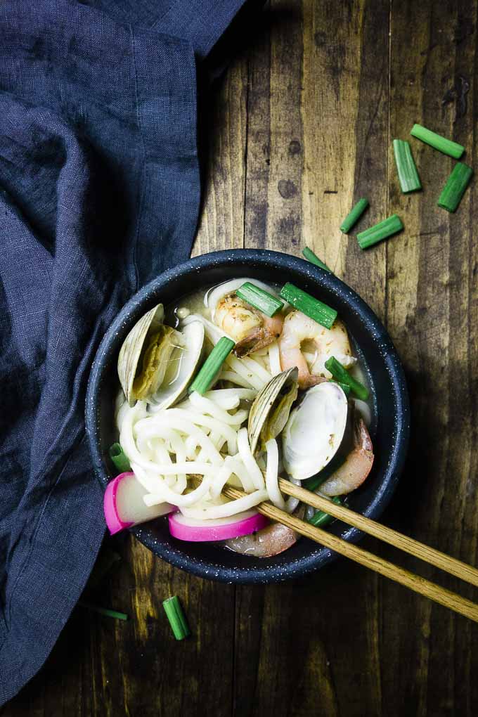 bowl of udon noodle soup with clams, shrimp and green onions with chopsticks