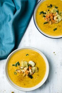 2 bowls of orange soup with crawfish and croutons on top