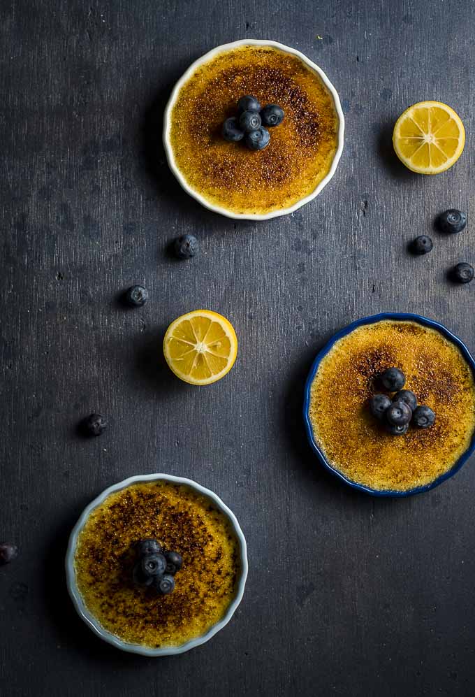 3 creme brulees on a surface with blueberries and lemon