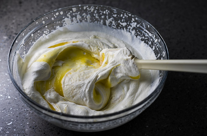 lemon curd being folded into whipped cream with a spatula