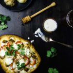 naan flatbread pizza with red peppers, chicken, cilantro and white sauce - roasted garlic in the background