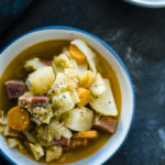 bowl of soup with carrots, potatoes and corned beef garnished with parsley