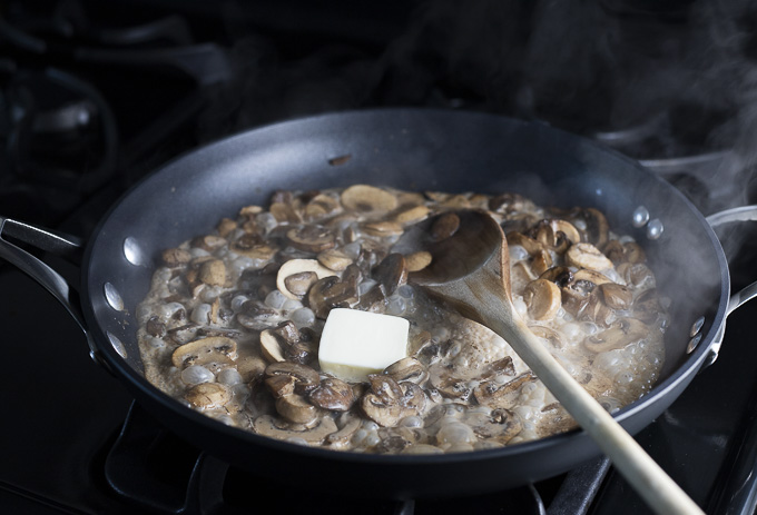 skillet of mushrooms cooking with a pad of butter