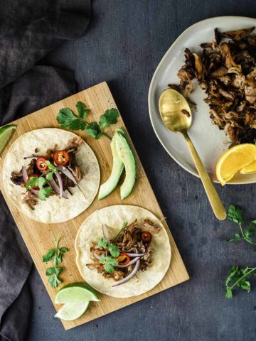 tacos on a board with a plate of shredded pork on the side