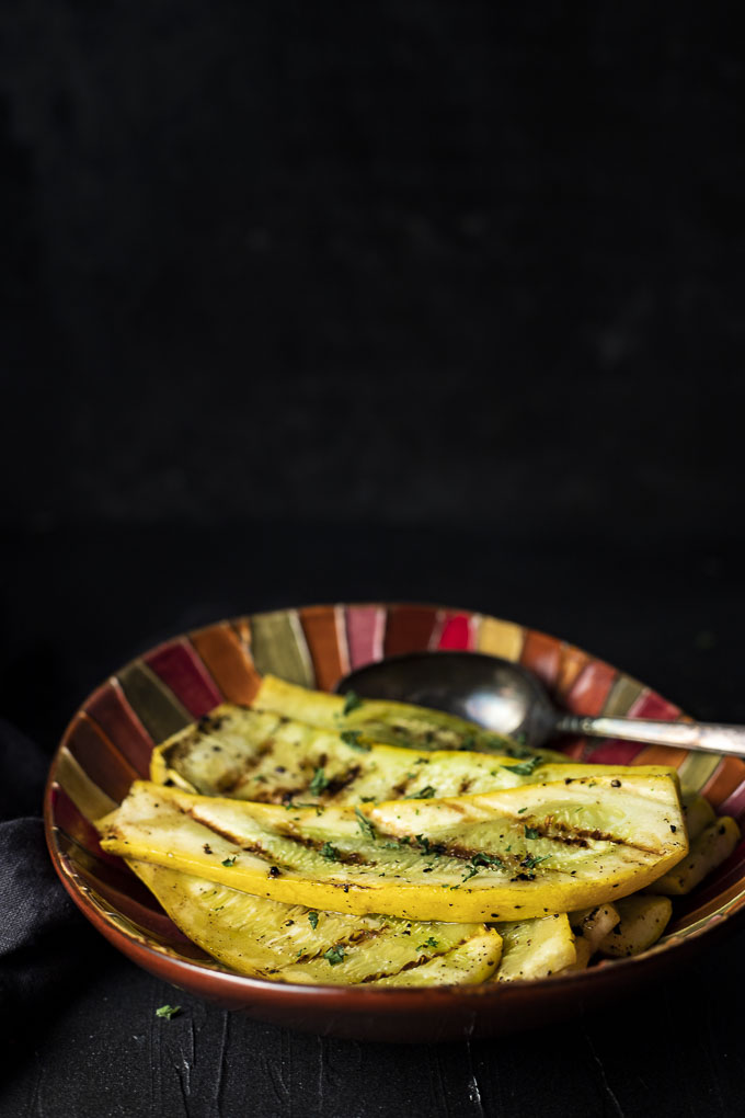 slices of grilled summer squash in a red dish with a spoo