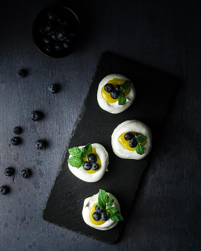 mini pavlovas on a plate with lemon and blueberries garnished with mint