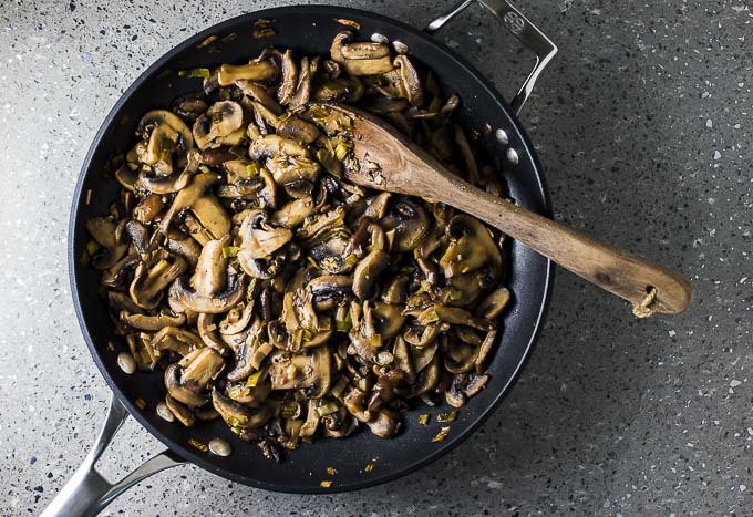 sauteed mushrooms in a skillet with a wooden spoon