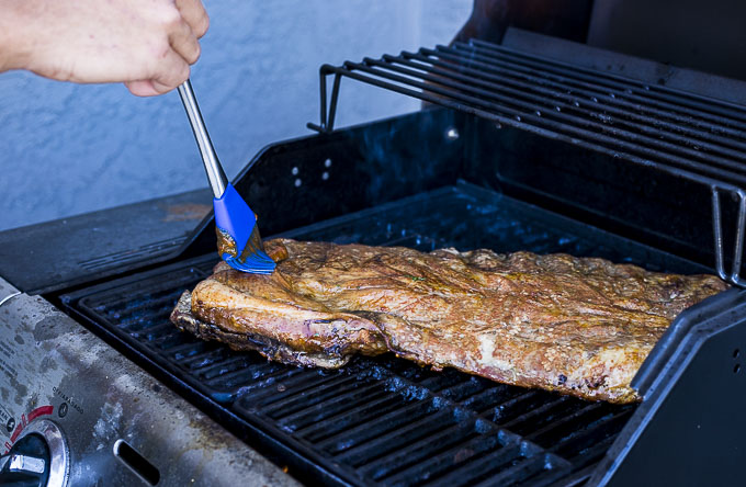 ribs being brushed with bbq sauce on a grill