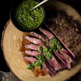 slices of flank steak drizzled in chimichurri (green sauce) with a bowl on the side