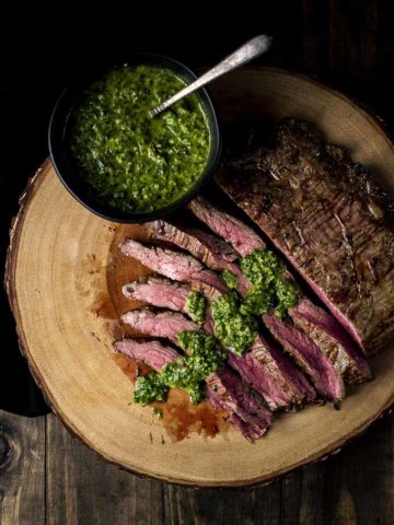 slices of flank steak drizzled in chimichurri (green sauce) with a bowl on the side