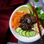seared beef in a bowl with cucumbers, carrots, basil, peanuts and limes