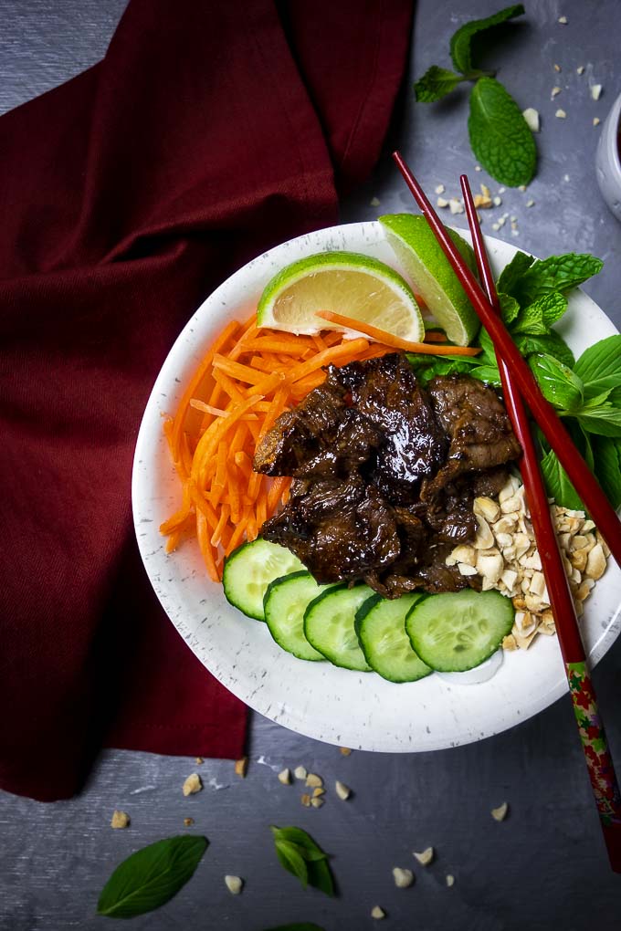 seared beef in a bowl with cucumbers, carrots, basil, peanuts and limes