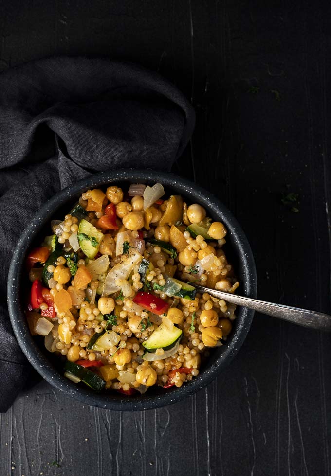 israeli couscous salad in a bowl with parsley and a spoon