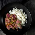 grilled beef slices and rice in a bowl with sauce and chives