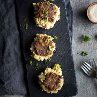 3 crabcakes on a serving platter with green onions on top - overhead view