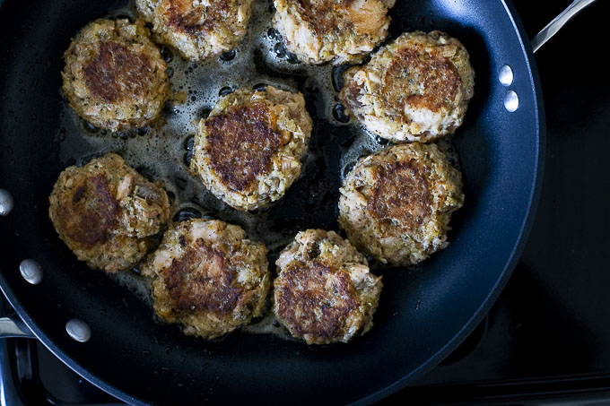 salmon cakes browned on one side cooking in a skillet
